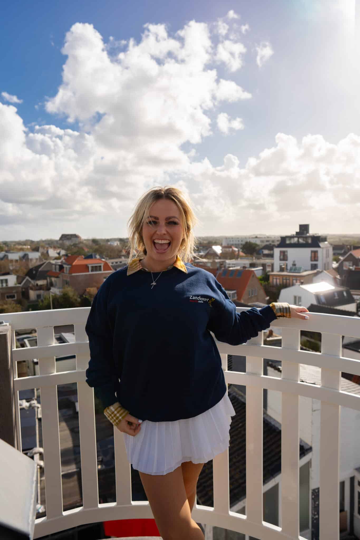 Vrouw staat lachend op het dakterras van Hotel Paradis met uitzicht over Zandvoort, genietend van haar overnachting.