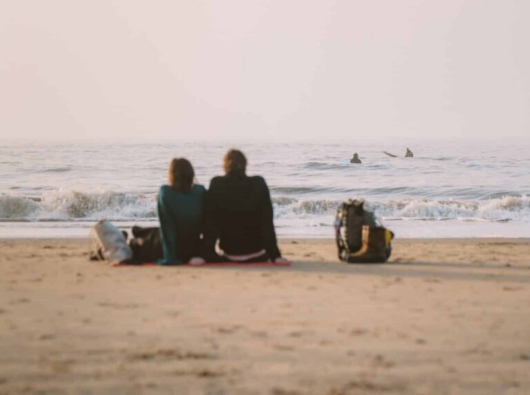 twee mensen zitten op het strand van Zandvoort te kijken naar watersporters