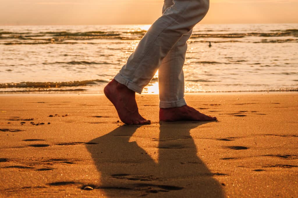 Voeten van een man die wandelt over het Zandvoortse strand bij zonsondergang