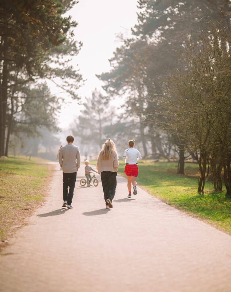 Wandelaars, een hardloper en een kind op een fiets delen een rustig pad door een groen natuurgebied met bomen aan weerszijden.