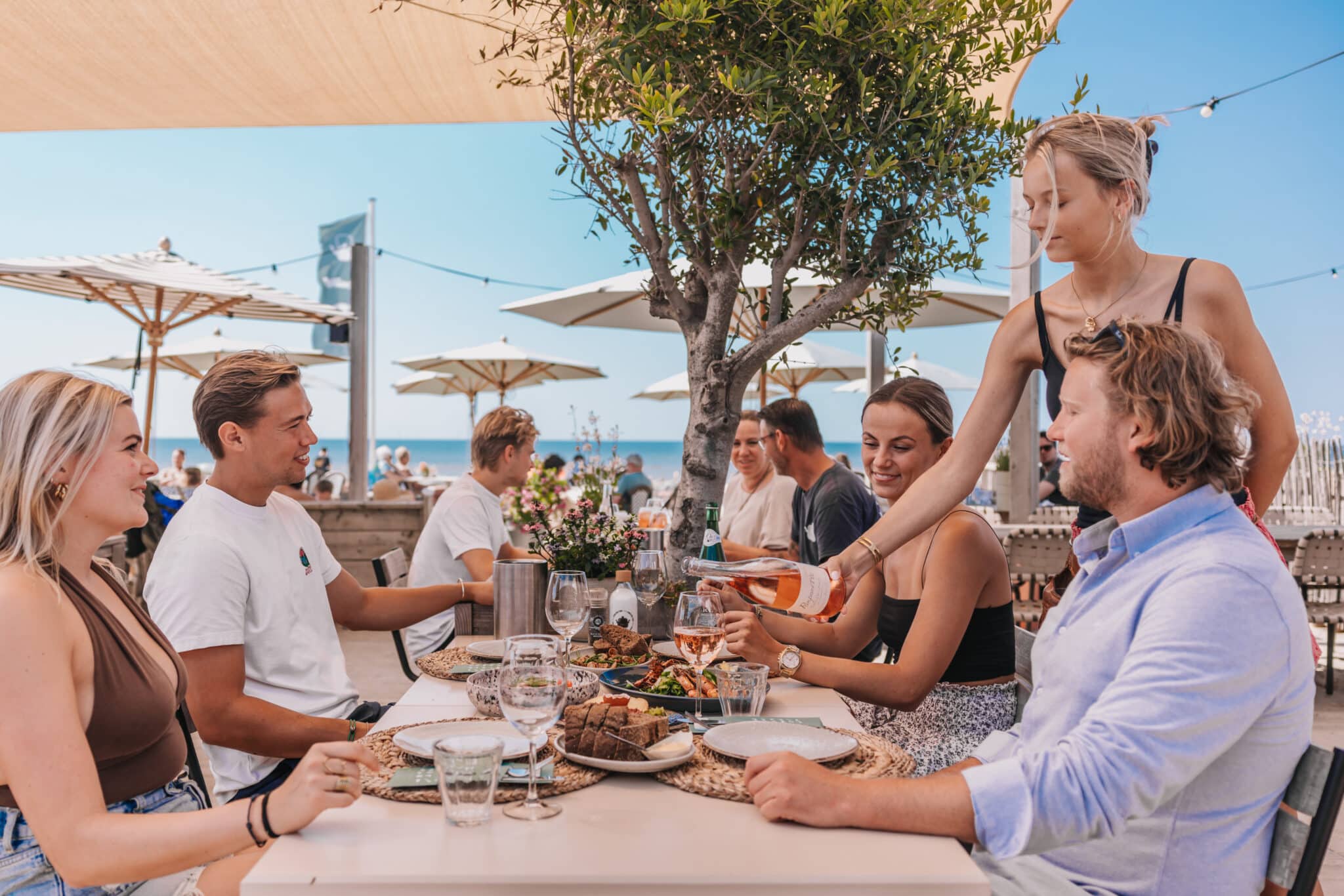 Gasten genieten van een diner op het terras van een strandpaviljoen in Zandvoort met uitzicht op het strand en de Noordzee.