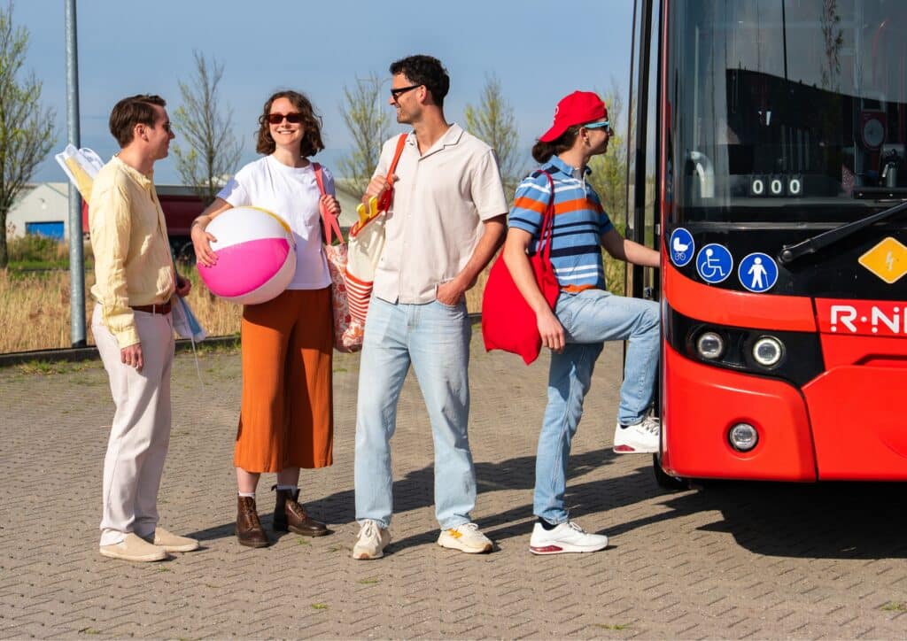 Vier strandbezoekers met strandspullen stappen op een rode Strandbus op weg naar het strand van Zandvoort.