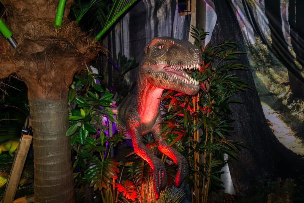 Animatronic velociraptor tussen tropische planten en bomen in de overdekte dinosaurusbeleving World of Dinos in Zandvoort.